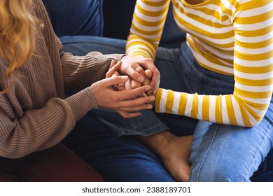 Midsection of biracial lesbian couple holding hands sitting on couch at home. Gay, love, relationship, togetherness, domestic life and lifestyle, unaltered. - Powered by Shutterstock