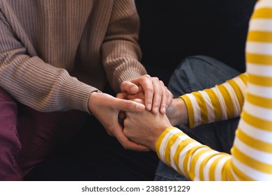 Midsection of biracial lesbian couple holding hands sitting on couch at home. Gay, love, relationship, togetherness, domestic life and lifestyle, unaltered. - Powered by Shutterstock