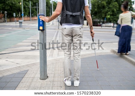 Midsection of blind man with white cane at pedestrain crossing in city.