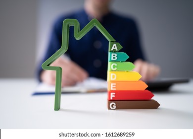 Midsection Of Businessman Calculating Invoice With Energy Efficient Chart On House Model In Office