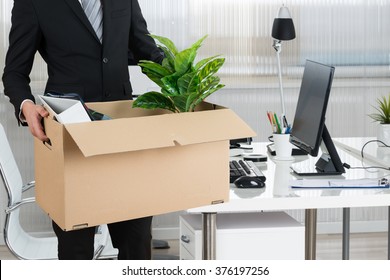 Midsection Of Businessman Carrying Cardboard Box By Desk In Office