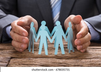 Midsection of businessman covering paper team with hands on wooden table - Shutterstock ID 678035731
