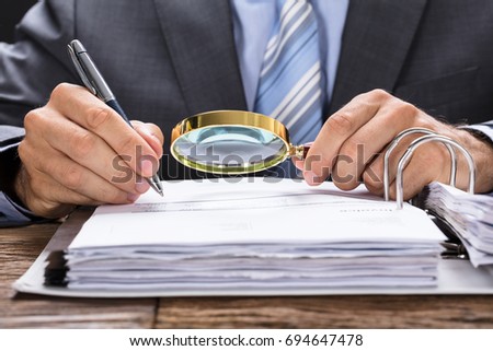 Midsection of businessman examining invoice with magnifying glass at desk