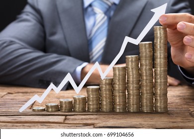 Midsection of businessman holding paper arrow on stacked coins arranged in increasing order on table - Shutterstock ID 699104656