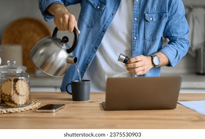 Midsection of businessman pouring hot water in coffee cup while using laptop on kitchen counter - Powered by Shutterstock