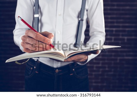 Midsection of businessman using cellphone while writing in his notebad at office