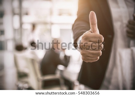 Midsection of businesswoman showing thumbs up sign in office with copy space
