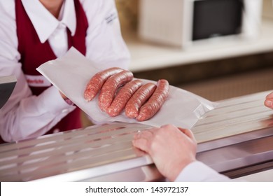 Midsection Of Butcher Displaying Sausages In Front Of Customer At Shop Counter