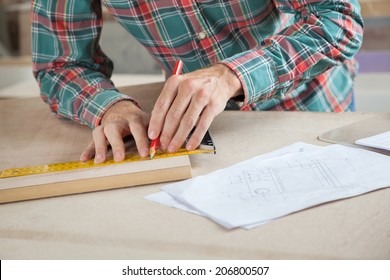 Midsection of carpenter measuring wood while marking in workshop