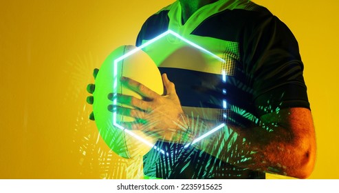 Midsection of caucasian male player holding rugby ball by hexagon and plants on yellow background. Hand, copy space, composite, sport, competition, shape, nature, illuminated and abstract concept. - Powered by Shutterstock