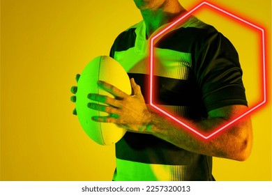 Midsection of caucasian male rugby player holding ball by illuminated hexagon over yellow background. Copy space, composite, sport, competition, shape, playing, hand, match and abstract concept. - Powered by Shutterstock