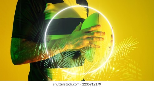 Midsection of caucasian rugby player holding ball by circle and plants over yellow background. Illuminated, hand, copy space, composite, sport, competition, shape, nature, playing, match and abstract. - Powered by Shutterstock