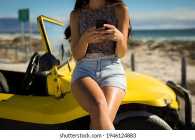 Midsection of caucasian woman sitting on beach buggy by the sea using smartphone. beach break on summer holiday road trip. - Powered by Shutterstock