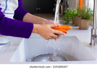 Midsection of caucasian woman standing in kitchen washing carrots in sink. Domestic life, food and healthy eating, spending time alone at home. - Powered by Shutterstock