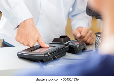 Midsection of customer giving thumb impression to make payment in pharmacy