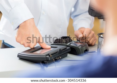 Midsection of customer giving thumb impression to make payment in pharmacy