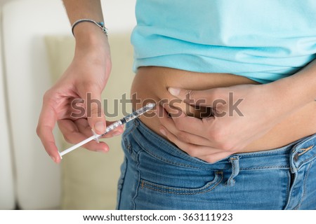 Midsection of diabetic young woman injecting stomach at home