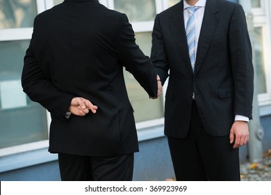 Midsection Of Dishonest Businessman With Fingers Crossed Shaking Hands With Partner Outdoors