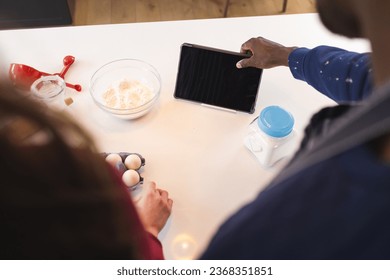 Midsection of diverse couple baking together in kitchen, using tablet with copy space at home. Lifestyle, togetherness, relationship, baking, recipe, communication and domestic life. - Powered by Shutterstock