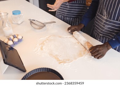 Midsection of diverse couple baking together in kitchen, using tablet at home. Lifestyle, togetherness, relationship, baking, recipe, communication and domestic life. - Powered by Shutterstock