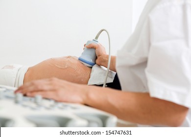 Midsection Of Doctor Examining Pregnant Belly By Ultrasonic Scan In Clinic