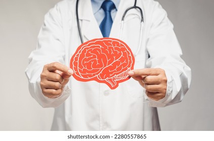 Midsection of a doctor in a uniform holding a brain symbol made from red paper while standing in the hospital. Dementia concept. Close-up photo. Space for text. Medical and healthcare