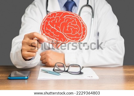 Midsection of a doctor in a uniform holding a brain symbol made from red paper while sitting at the table in the hospital. Close-up photo. Medical and healthcare concept