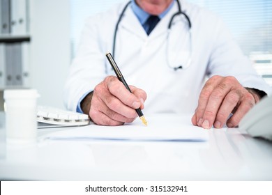 Midsection Of Doctor Writing On Paper At Clinic