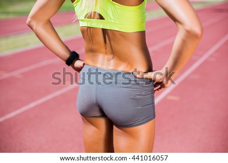 Mid-section of female athlete standing with hand on hip on a running track
