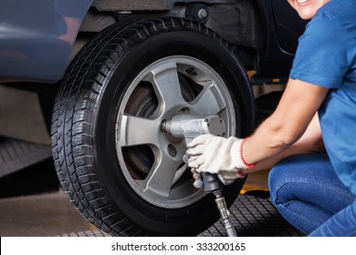 Midsection of female mechanic using pneumatic wrench to fix car tire at repair shop - Powered by Shutterstock