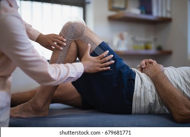 Midsection of female therapist measuring knee while senior male patient lying on bed at hospital ward - Powered by Shutterstock