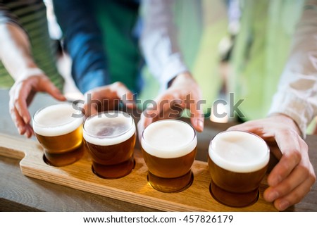 Midsection of friends reaching towards beer sampler at bar counter