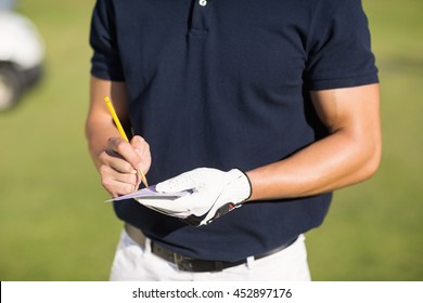 Midsection of golfer writing on score card while standing at golf course - Powered by Shutterstock