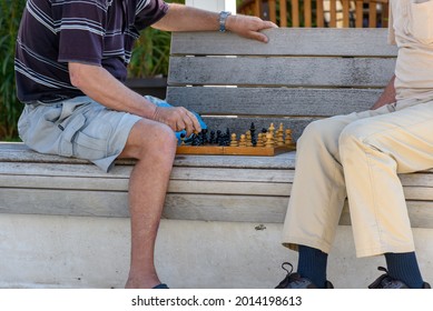 Mid-section image of two old men playing chess on bench in city 