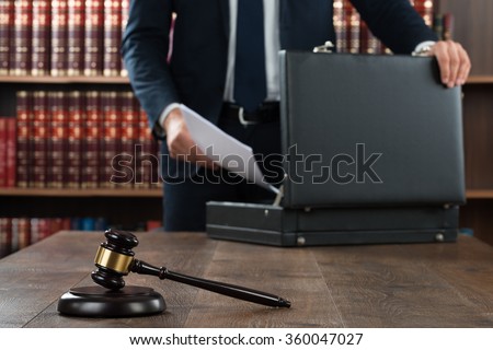 Midsection of lawyer putting documents in briefcase with gavel at desk in courtroom