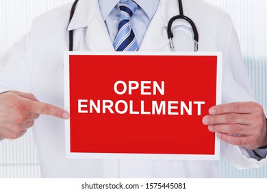 Midsection Of A Male Doctor Pointing At Open Enrollment Text On Placard Holding In Hand