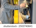 Midsection of male entrepreneur operating modern coffeemaker while standing in office during break