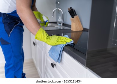 Midsection Of Male Janitor Cleaning Kitchen Counter With Detergent Spray Bottle And Sponge