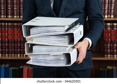 Midsection of male lawyer carrying stack of ring binders in courtroom