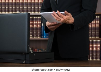 Midsection of male lawyer keeping documents in briefcase at table in office