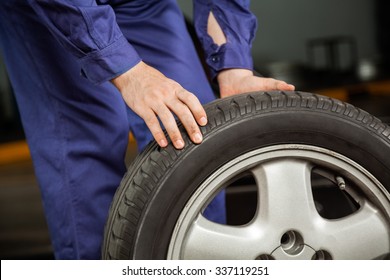 Midsection Of Male Mechanic Holding Car Tire At Garage