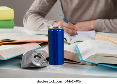 Midsection of male student studying with crashed drink can and books at table