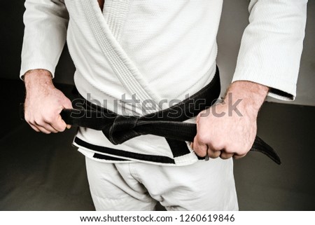 Midsection of Man in A Gi holding Black Belt tied Around His Waist. 