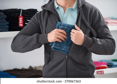 Midsection of man hiding jeans in jacket at store