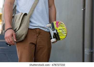 Midsection of man holding skateboard while walking by wall
