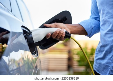 Midsection of man plugging in cable while charging electric car: stockfoto