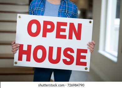 Mid-section of man standing in the living room holding open sign 