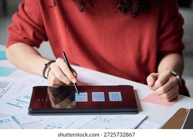 Midsection of man using digital pen to design mobile app interface on tablet, working at desk with paper wireframes and mockups, focusing on creative process in modern workspace