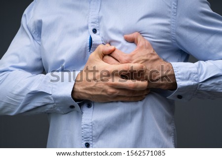 Midsection Of A Man Wearing Blue Shirt Suffering From Heart Attack Standing Against Grey Background