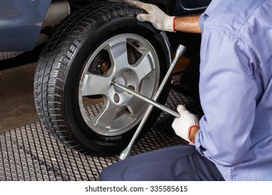 Midsection Of Mechanic Fixing Car Tire With Rim Wrench At Repair Shop